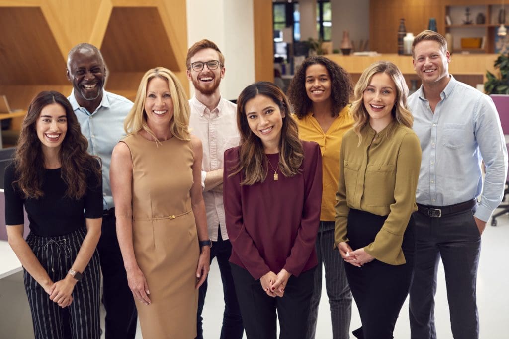 Portrait Of Smiling Multi-Cultural Business Team Standing In Modern Open Plan Office